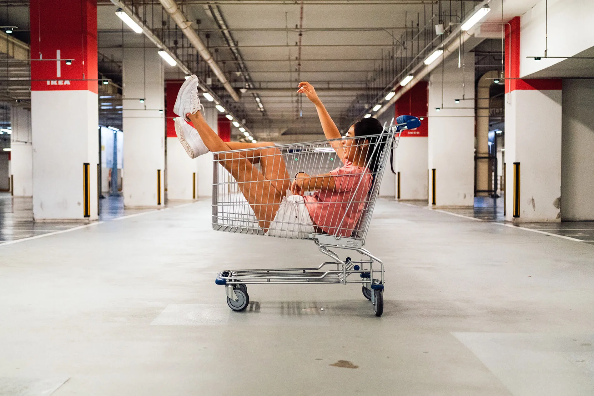 Woman in shopping cart in the middle of an empty warehouse
