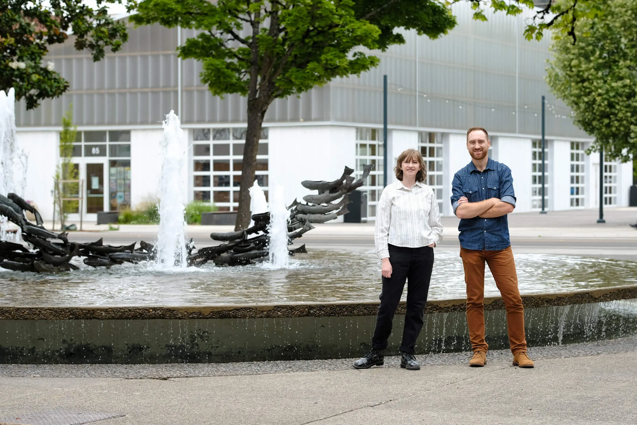 Sterner Stuff owner Ethan Clevenger and associate developer Maddy Harrison pose in front of the water feature in the Park Blocks in Downtown Eugene, Oregon. The Farmers Market Pavilion can be seen in the background.